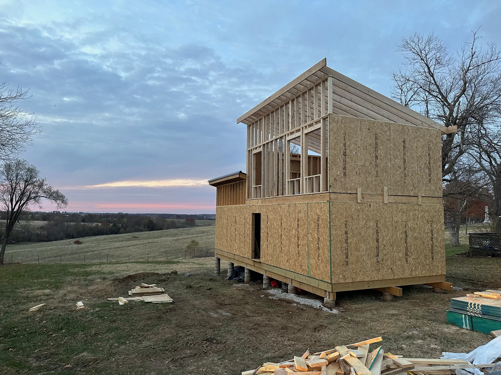 The framed house standing at dusk with open fields behind it.